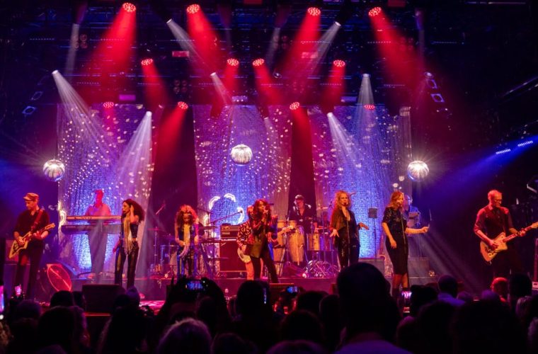 Zangeres Irma Derby in glitteroutfit, staand op het podium van Schouwburg Hengelo, omgeven door liveband – tribute aan Donna Summer.